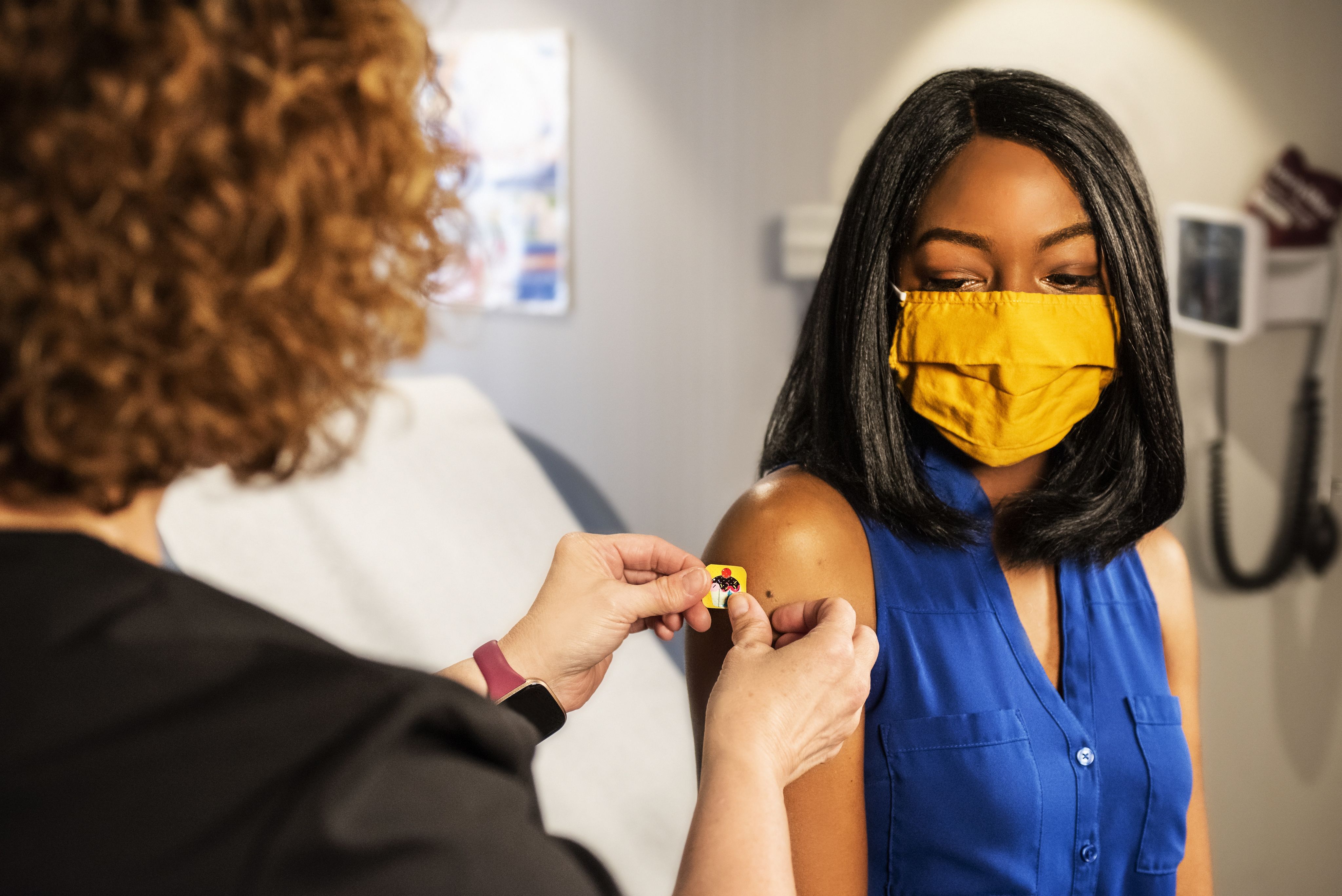 a nurse applies a plaster after administering a vaccination to a woman in a blue shirt