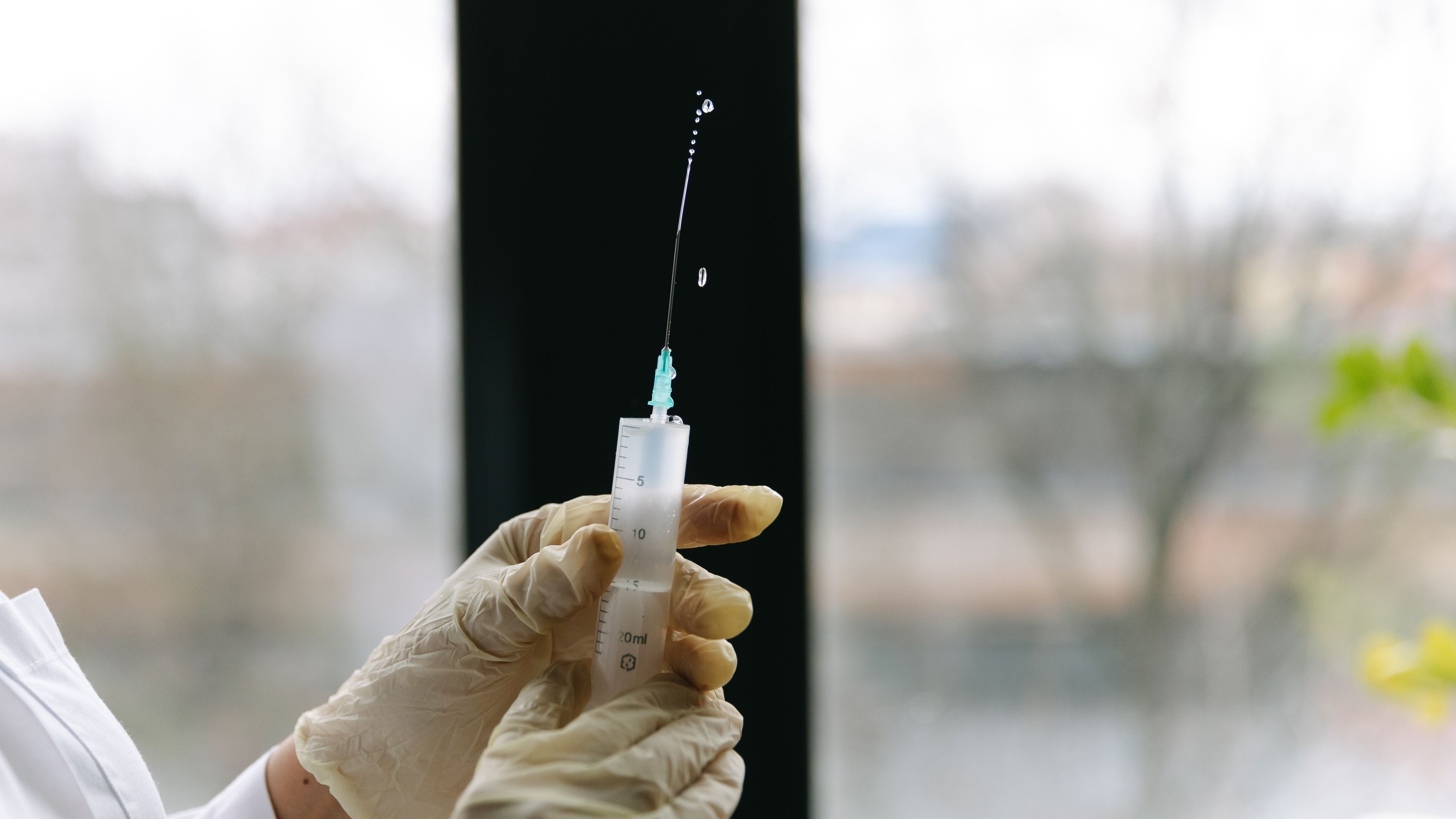 A photograph of a doctor's hands checking a syringe and needle are full before administering an injection