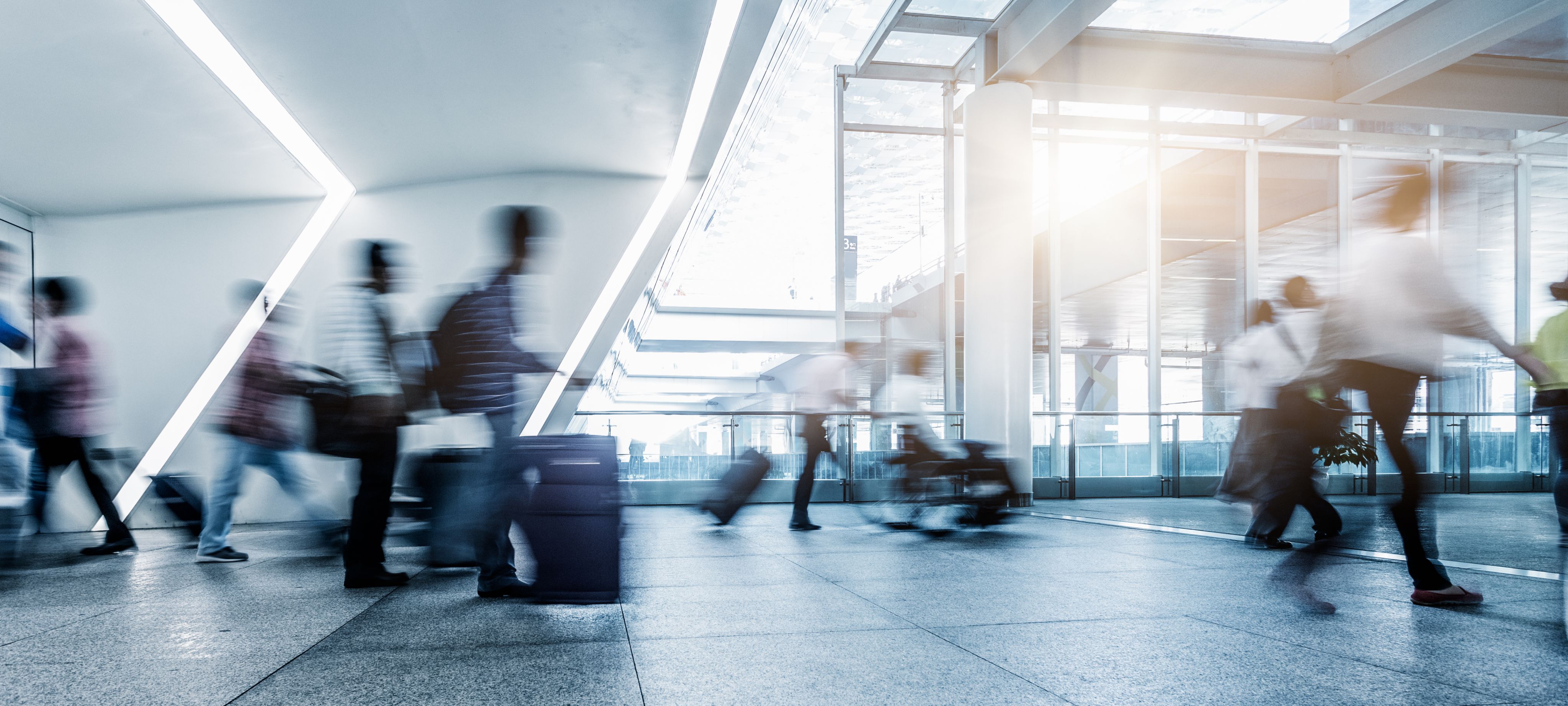 A photograph of passengers rushing through an airport. The passenger images are blurred to create an impression of speed
