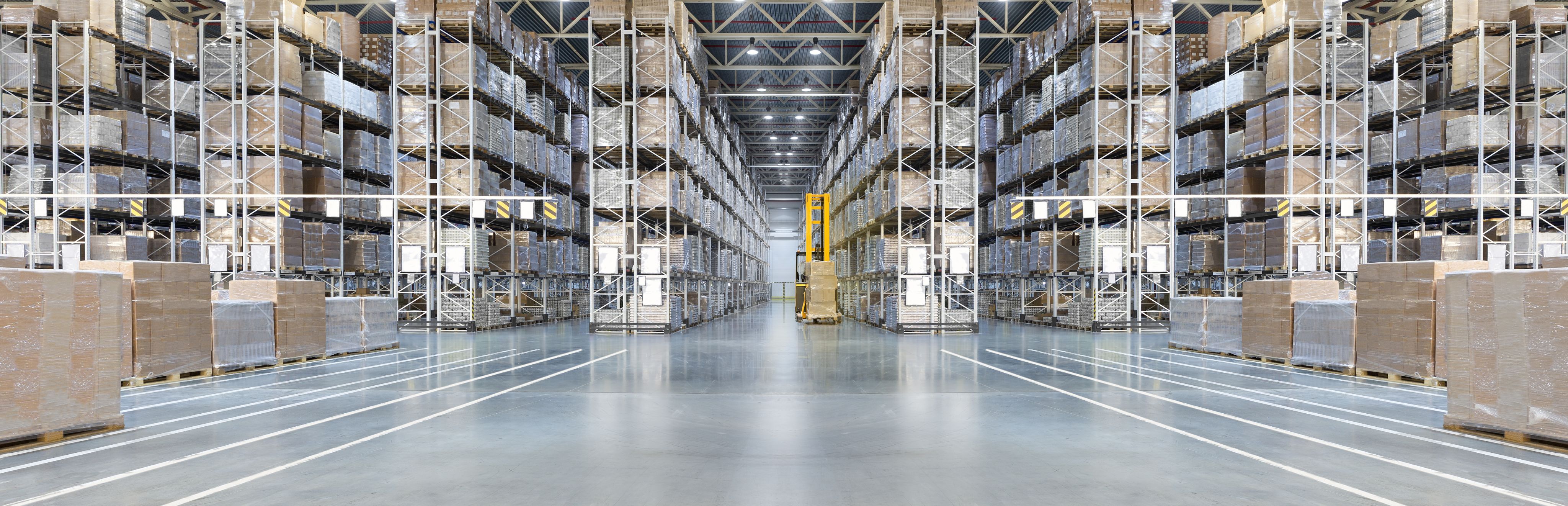 A photograph of a large warehouse with floor to ceiling racks full of products and a yellow forklift truck in the centre aisle
