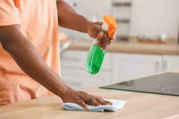 Man using a cleaning spray to wipe a kitchen surface