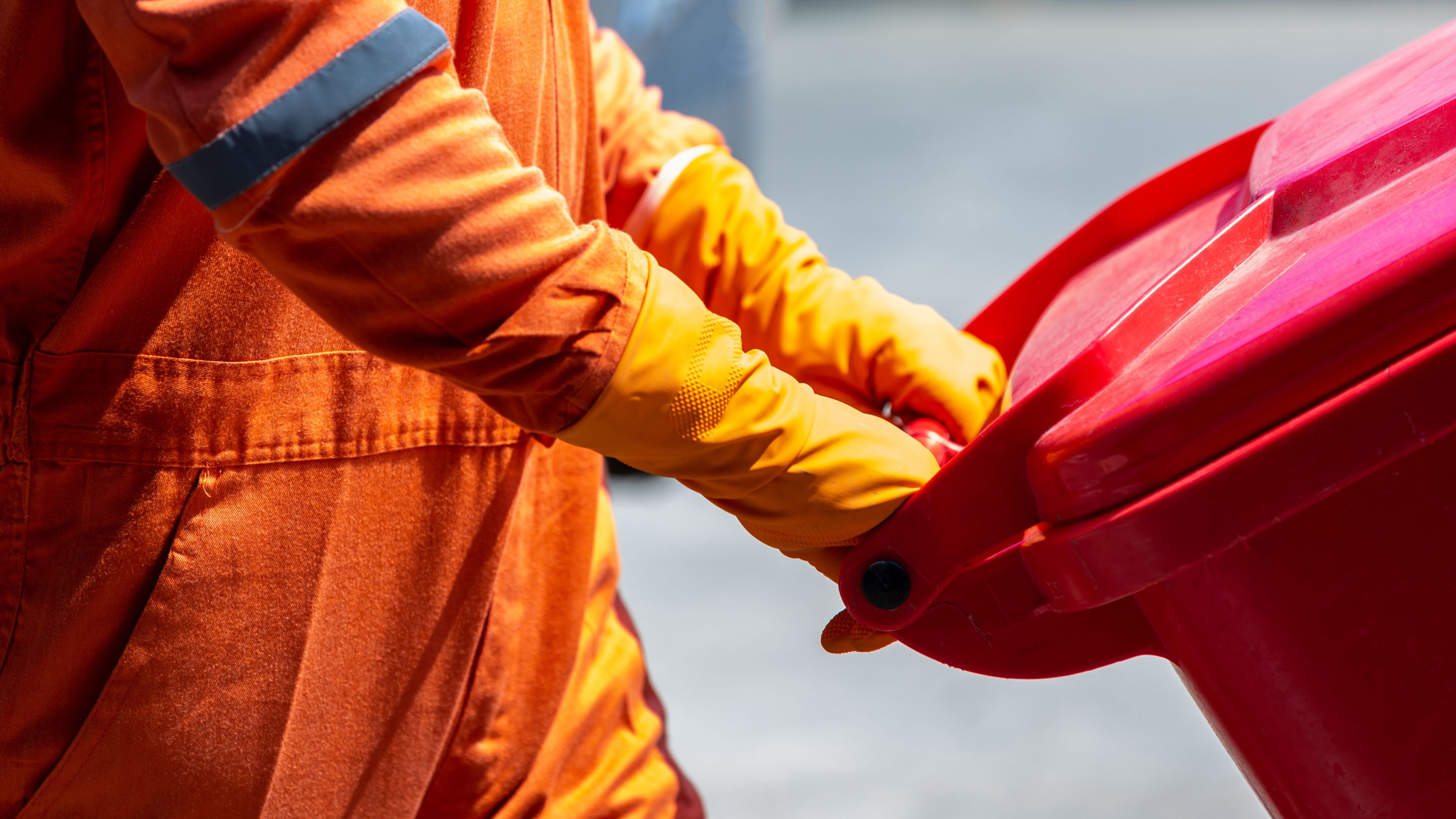 Bin person in orange outfit wheels red wheelie bin