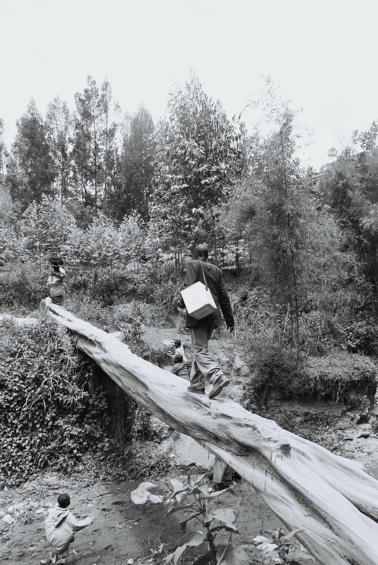 Man walks across a river on balancing on a log, carrying a medical box