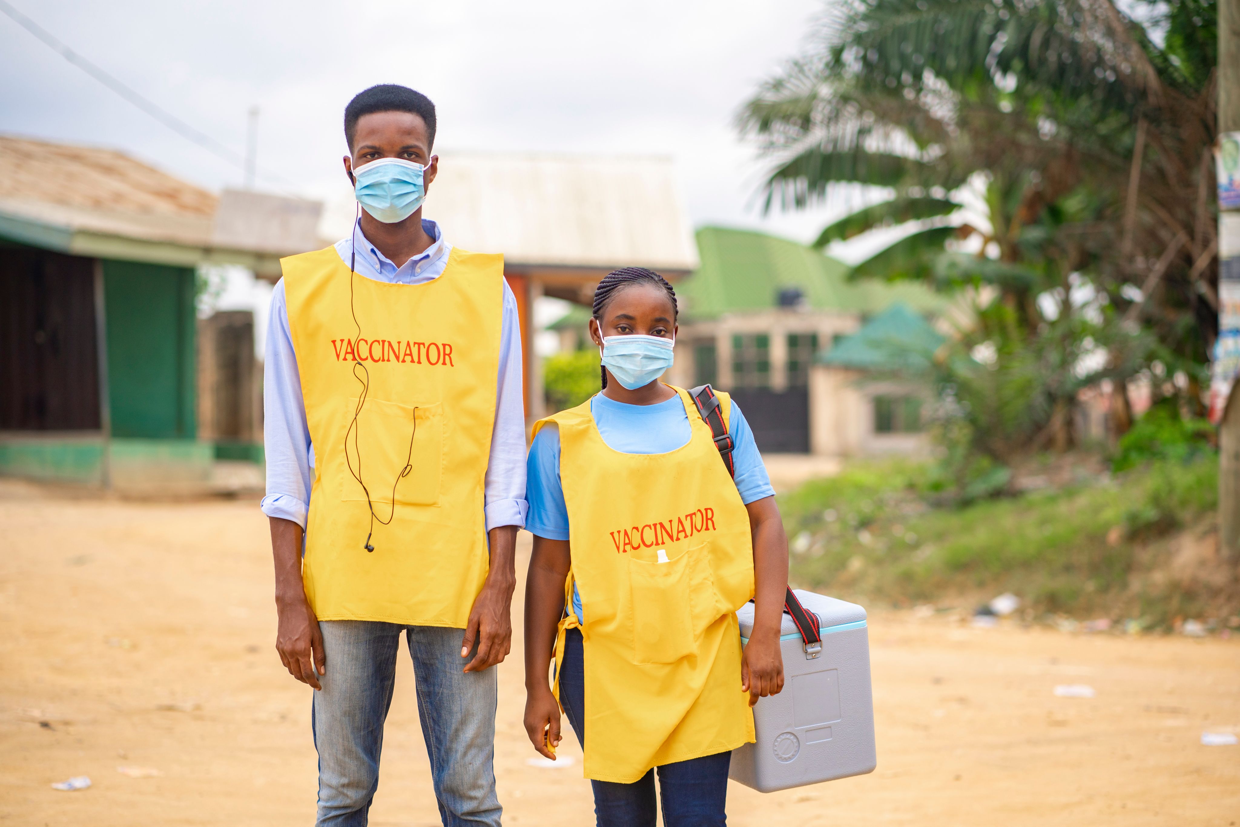 Two healthcare workers in hot country wearing 'vaccinator' bibs